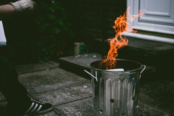 A stainless steel trash can outside with flames and smoke, creating a dramatic scene.